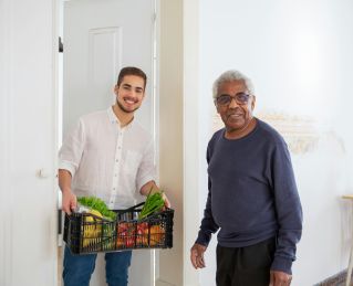 Senior man receiving fresh produce from a young volunteer indoors, promoting community support.